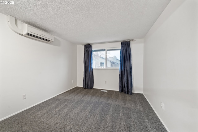 empty room featuring baseboards, a textured ceiling, dark carpet, and an AC wall unit