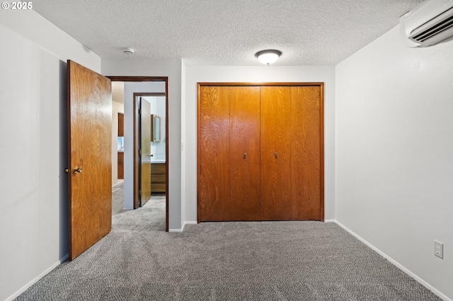 unfurnished bedroom with a wall unit AC, carpet, and a textured ceiling