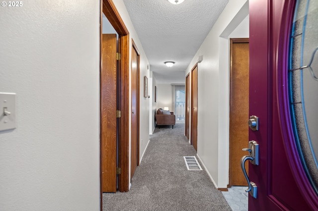 hallway featuring a textured ceiling, baseboards, visible vents, and light colored carpet