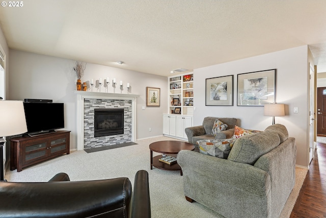 living area with a tiled fireplace, baseboards, built in shelves, and a textured ceiling