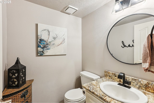 half bath with vanity, a textured ceiling, and toilet