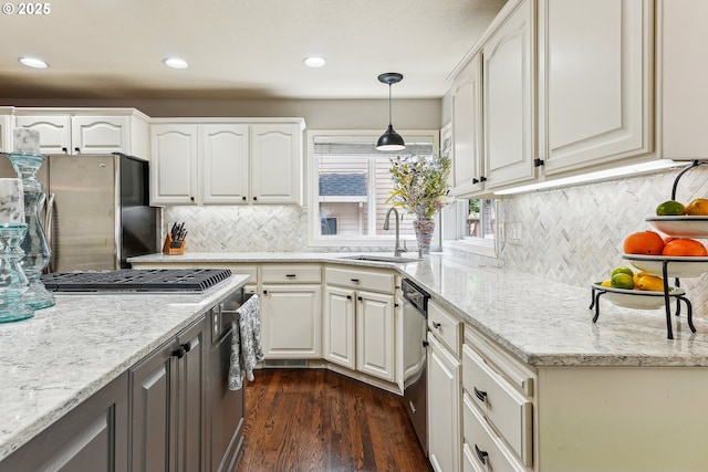 kitchen featuring light stone countertops, a sink, dark wood finished floors, appliances with stainless steel finishes, and decorative light fixtures