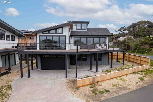 rear view of house with board and batten siding, a garage, driveway, and a patio area