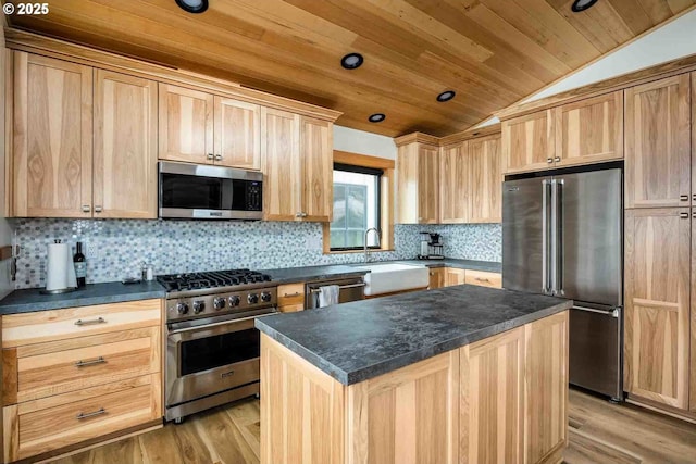 kitchen featuring premium appliances, light brown cabinetry, lofted ceiling, a sink, and dark countertops