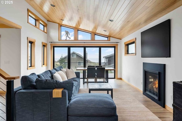 living room featuring wooden ceiling, wood finished floors, a glass covered fireplace, healthy amount of natural light, and vaulted ceiling