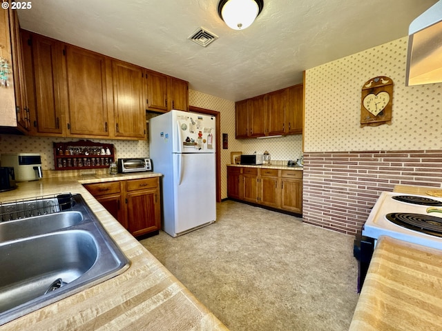 330 Maple St, Brookings, OR 97415 - kitchen with freestanding refrigerator, wallpapered walls, brown cabinetry, and range with electric cooktop