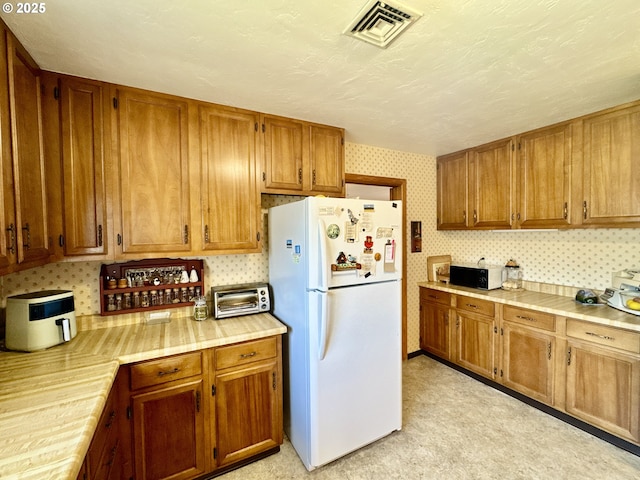 330 Maple St, Brookings, OR 97415 - kitchen with freestanding refrigerator, light countertops, brown cabinetry, and wallpapered walls