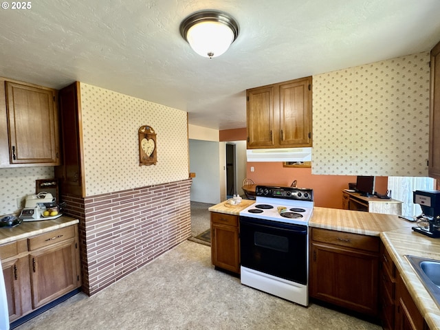 330 Maple St, Brookings, OR 97415 - kitchen with range with electric stovetop, under cabinet range hood, wallpapered walls, light countertops, and light carpet