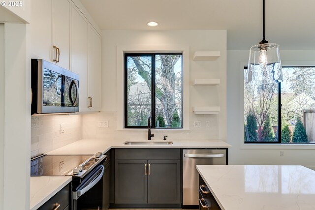 kitchen featuring sink, white cabinets, hanging light fixtures, stainless steel appliances, and light stone countertops