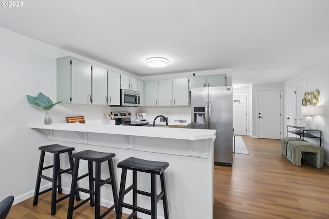 kitchen with a breakfast bar, a peninsula, light countertops, appliances with stainless steel finishes, and wood finished floors