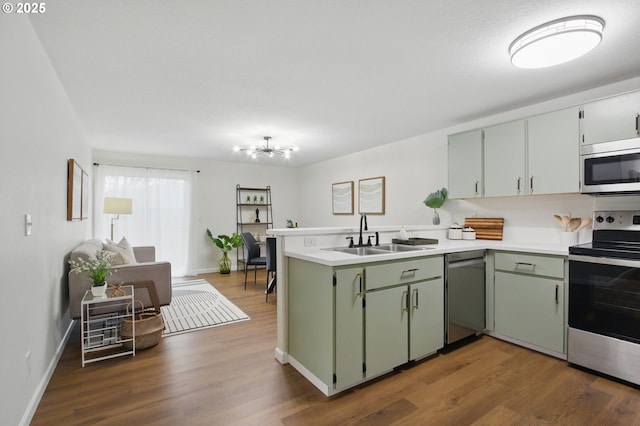 kitchen featuring green cabinets, a peninsula, appliances with stainless steel finishes, light countertops, and a sink
