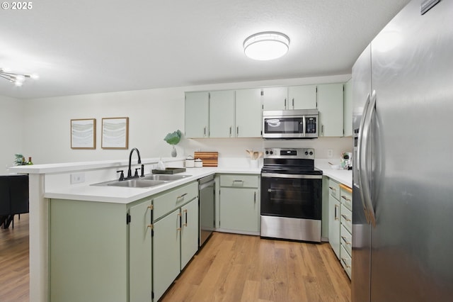 kitchen with light wood-type flooring, a peninsula, light countertops, appliances with stainless steel finishes, and a sink