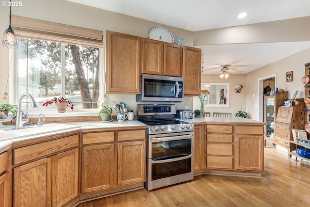 kitchen with a sink, light countertops, appliances with stainless steel finishes, light wood-type flooring, and pendant lighting