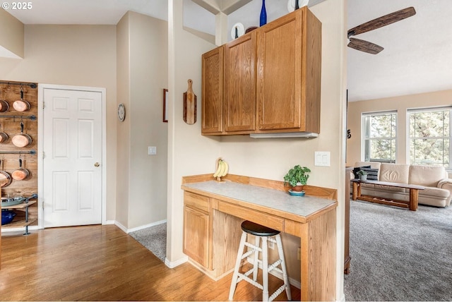 kitchen with wood finished floors, a ceiling fan, baseboards, light countertops, and brown cabinetry