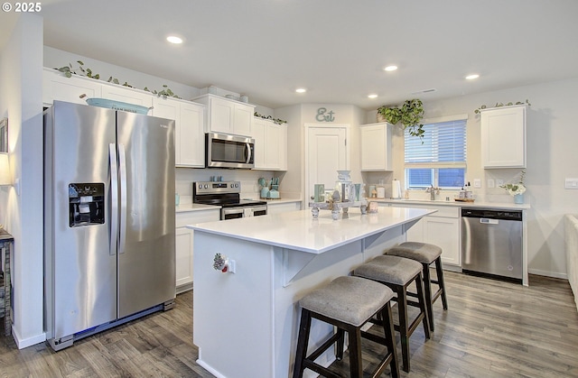 kitchen with a kitchen island, white cabinets, a kitchen breakfast bar, stainless steel appliances, and dark wood-type flooring