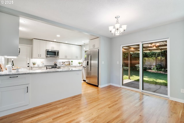 9885 SW Bonnie Brae Dr, Beaverton, OR 97008 - kitchen featuring stainless steel appliances, light wood-style flooring, a chandelier, white cabinetry, and tasteful backsplash