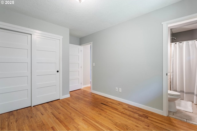 9885 SW Bonnie Brae Dr, Beaverton, OR 97008 - unfurnished bedroom featuring light wood finished floors, baseboards, a closet, ensuite bathroom, and a textured ceiling