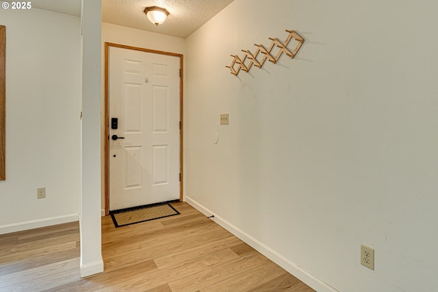 foyer entrance with a textured ceiling, baseboards, and light wood-style flooring