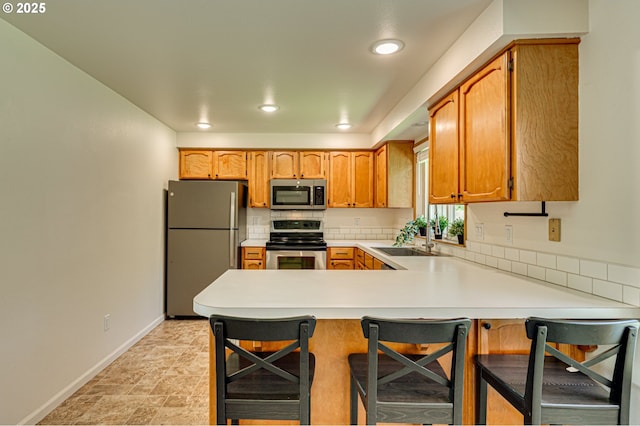 kitchen with a breakfast bar, a sink, stainless steel appliances, baseboards, and a peninsula