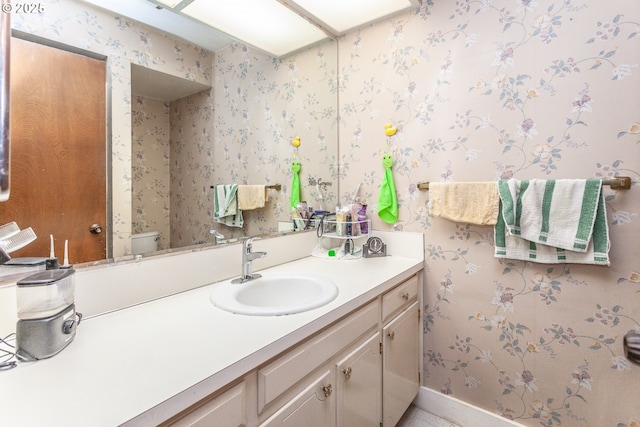 bathroom with wallpapered walls, toilet, vanity, and baseboards