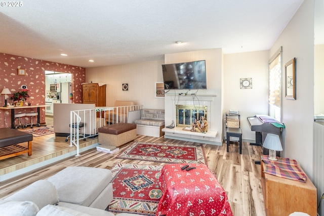 living room featuring a textured ceiling, wood finished floors, wallpapered walls, baseboards, and a tile fireplace