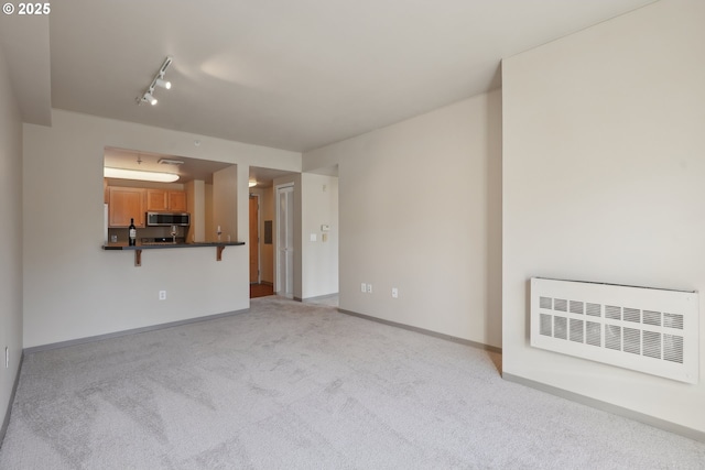 unfurnished living room with heating unit, light colored carpet, and rail lighting