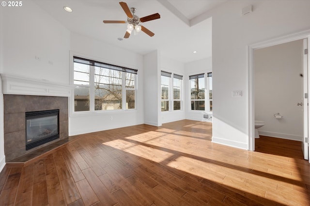 unfurnished living room featuring a tiled fireplace, a healthy amount of sunlight, hardwood / wood-style floors, and ceiling fan