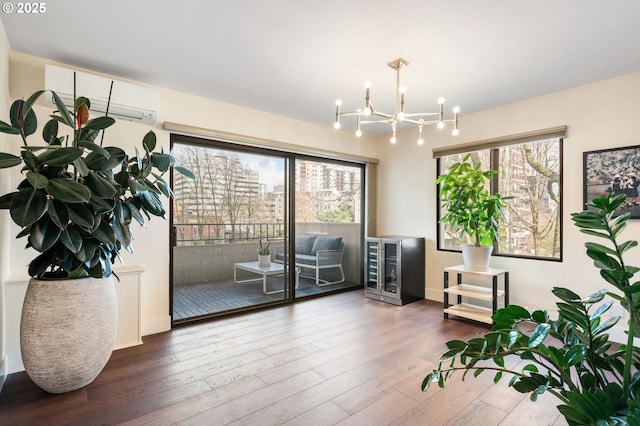 living area with a wealth of natural light, a notable chandelier, an AC wall unit, and wood finished floors