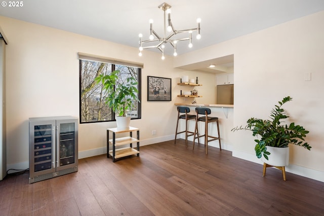 sitting room with baseboards, wine cooler, a notable chandelier, and wood finished floors