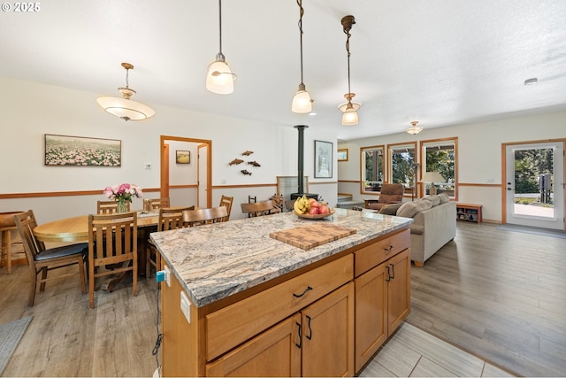 66020 Meissner Rd, Deer Island, OR 97054 - kitchen with a wood stove, a kitchen island, hanging light fixtures, light wood-style floors, and light stone countertops
