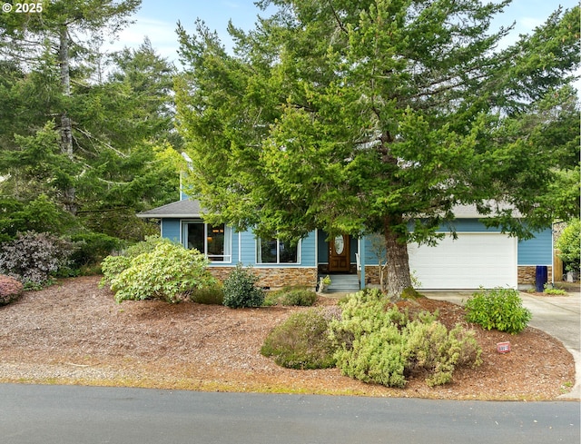 view of property hidden behind natural elements featuring stone siding, driveway, and a garage