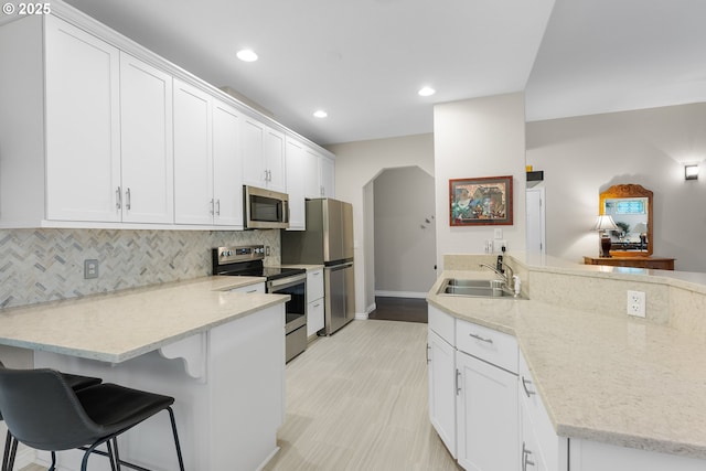 kitchen featuring a sink, stainless steel appliances, backsplash, and a peninsula