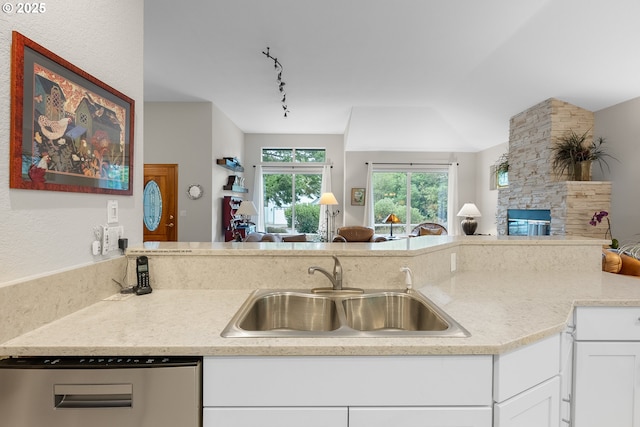 kitchen with a fireplace, a sink, white cabinets, stainless steel dishwasher, and open floor plan