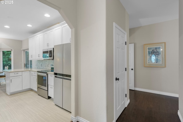 kitchen with baseboards, light countertops, a peninsula, stainless steel appliances, and white cabinetry