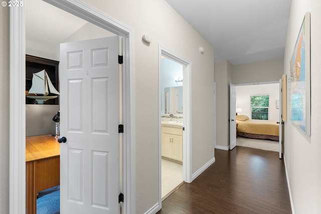 hallway with a sink, baseboards, and dark wood-style flooring