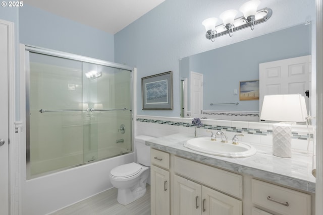 bathroom with vanity, tile walls, toilet, and bath / shower combo with glass door