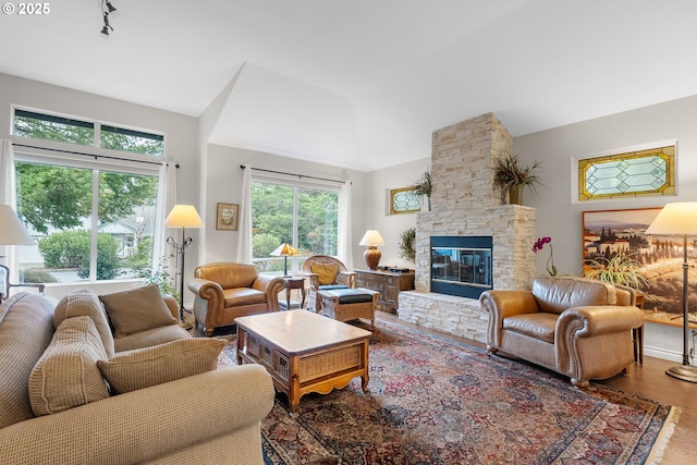 living area featuring vaulted ceiling, a stone fireplace, and wood finished floors