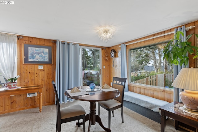 dining area featuring light carpet, plenty of natural light, and wooden walls