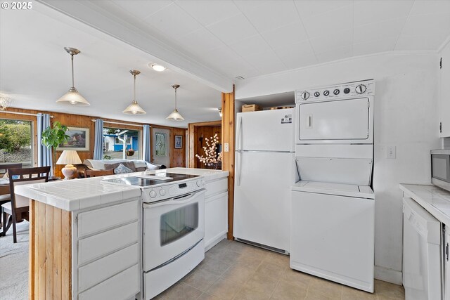 kitchen featuring white appliances, a peninsula, white cabinets, stacked washer / dryer, and tile counters