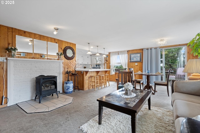 living room with wooden walls, a wood stove, light carpet, and a healthy amount of sunlight