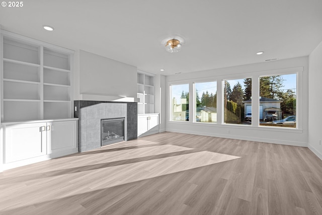 unfurnished living room with built in shelves, a fireplace, and light wood-type flooring