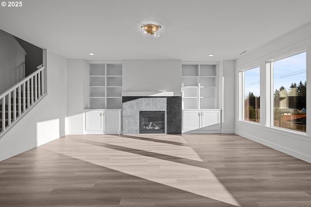 unfurnished living room featuring a tile fireplace, built in features, and light wood-type flooring