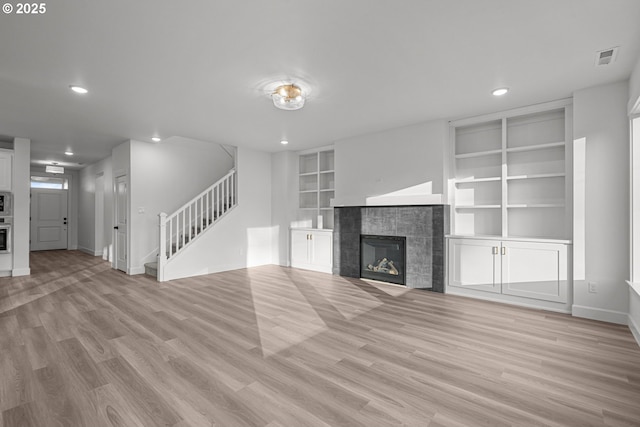 unfurnished living room with built in shelves, light hardwood / wood-style floors, and a tile fireplace