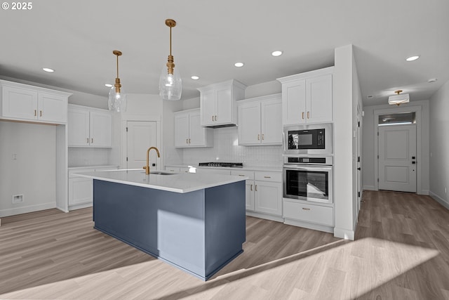 kitchen featuring appliances with stainless steel finishes, pendant lighting, sink, white cabinets, and a kitchen island with sink