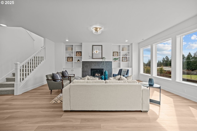 living room with built in shelves, baseboards, stairs, light wood-style flooring, and a fireplace