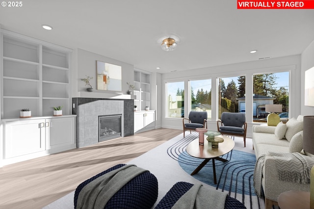 living room with built in shelves, a fireplace, and light hardwood / wood-style floors