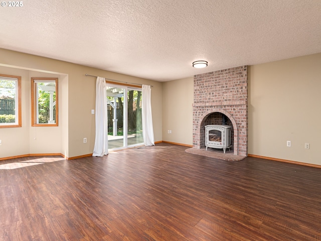 unfurnished living room featuring a textured ceiling, baseboards, a wood stove, and wood finished floors