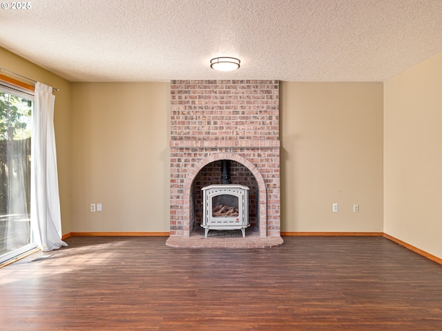 unfurnished living room with a textured ceiling, baseboards, a wood stove, and wood finished floors