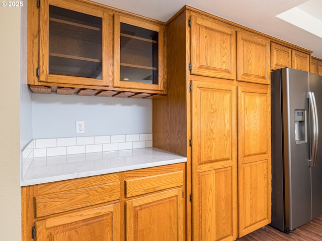 kitchen featuring brown cabinets, light countertops, stainless steel refrigerator with ice dispenser, dark wood-style floors, and glass insert cabinets