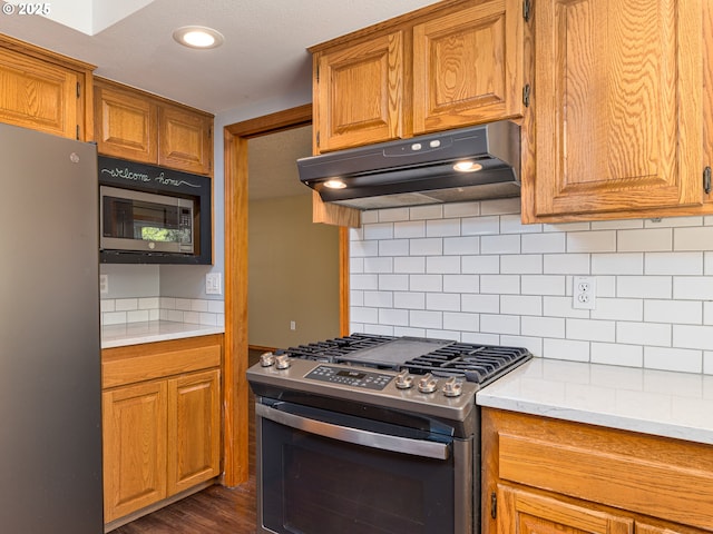kitchen with under cabinet range hood, stainless steel appliances, brown cabinetry, and light countertops